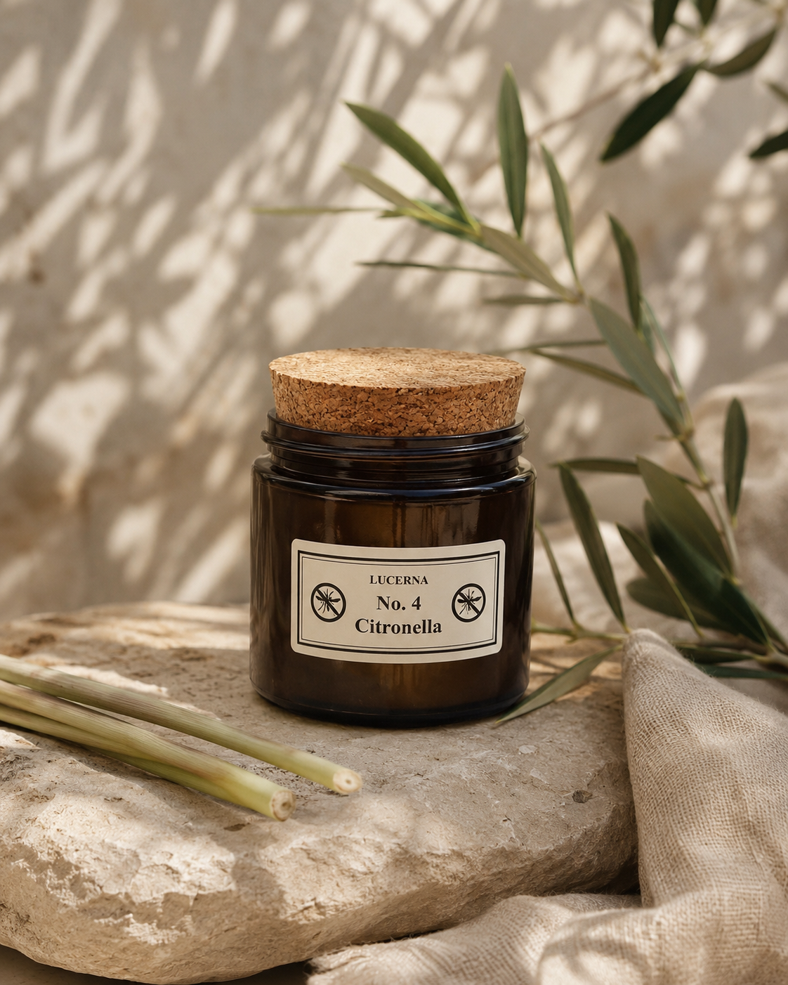 Lucerna Citronella Duftkerze 80 g im Braunglas mit Korkdeckel auf Naturstein mit Zitronengras und Olivenzweigen als natürlicher Mückenschutz für Balkon und Terrasse.